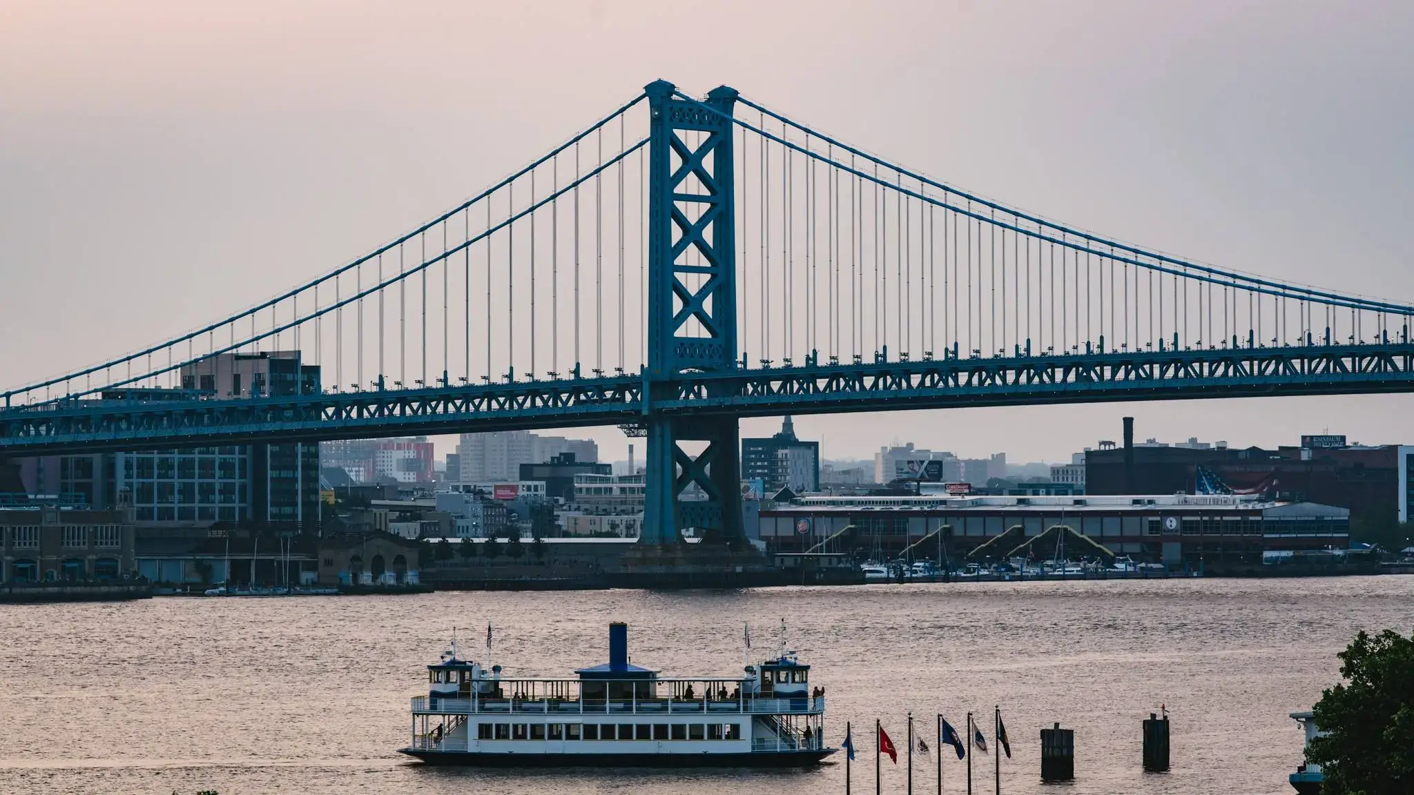 A ferry crosses the river near a large bridge to drop passengers at Freedom Mortgage Pavilion.