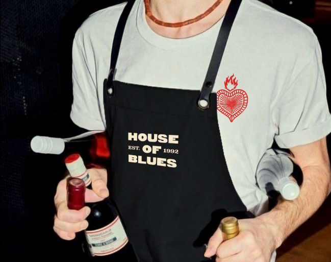 A person wearing a House of Blues tee shirt and apron holding bottles