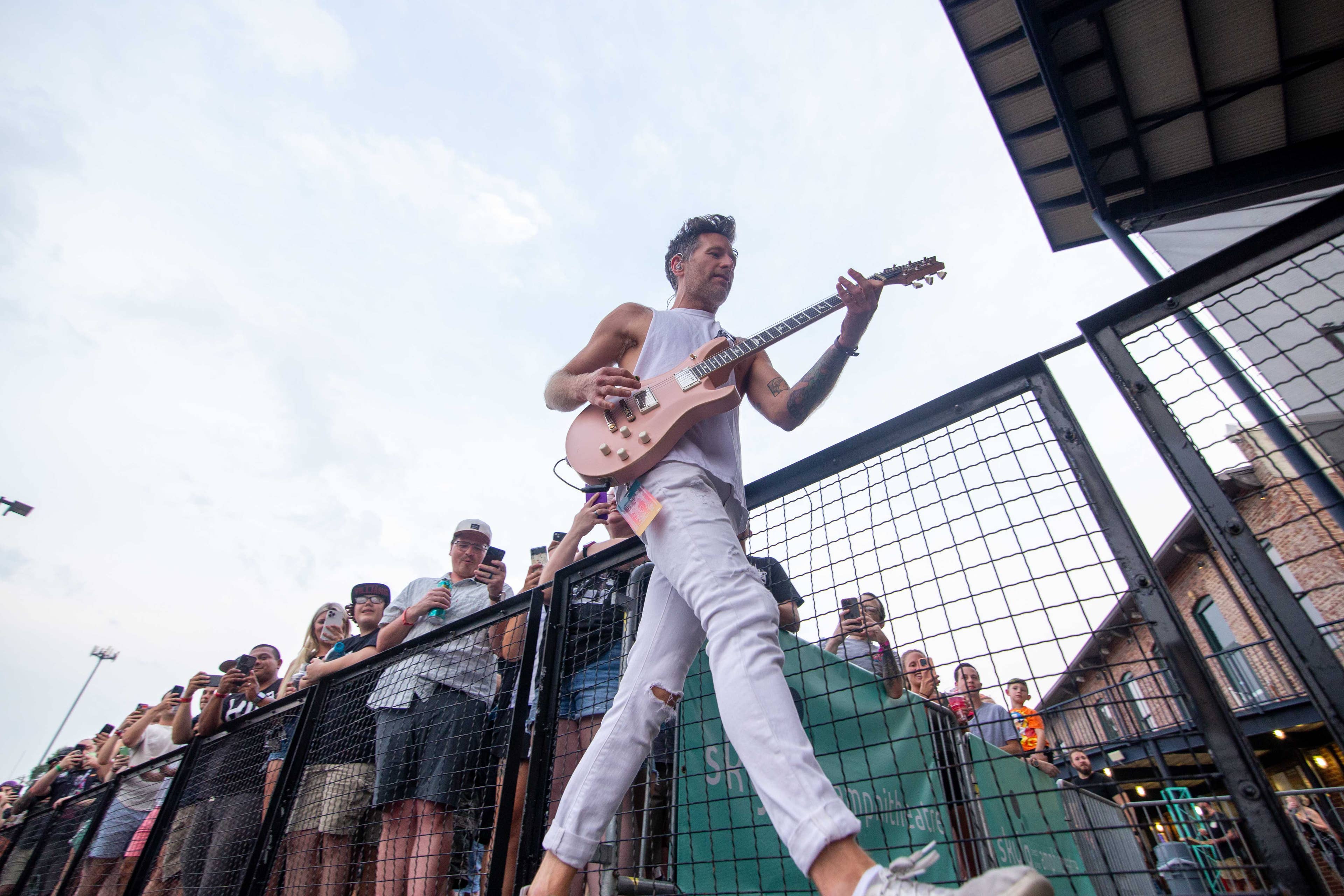A male guitar playing walking in front of fans on the railing. 