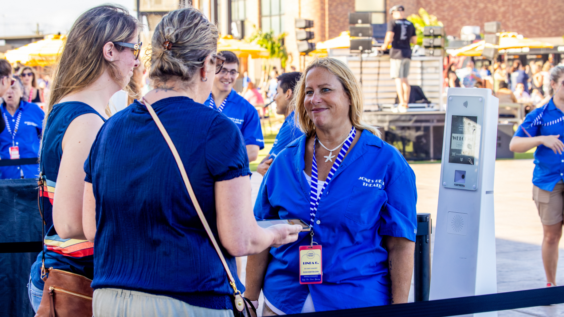 An employee with two fans at a ticket scanner, helping them enter the venue.