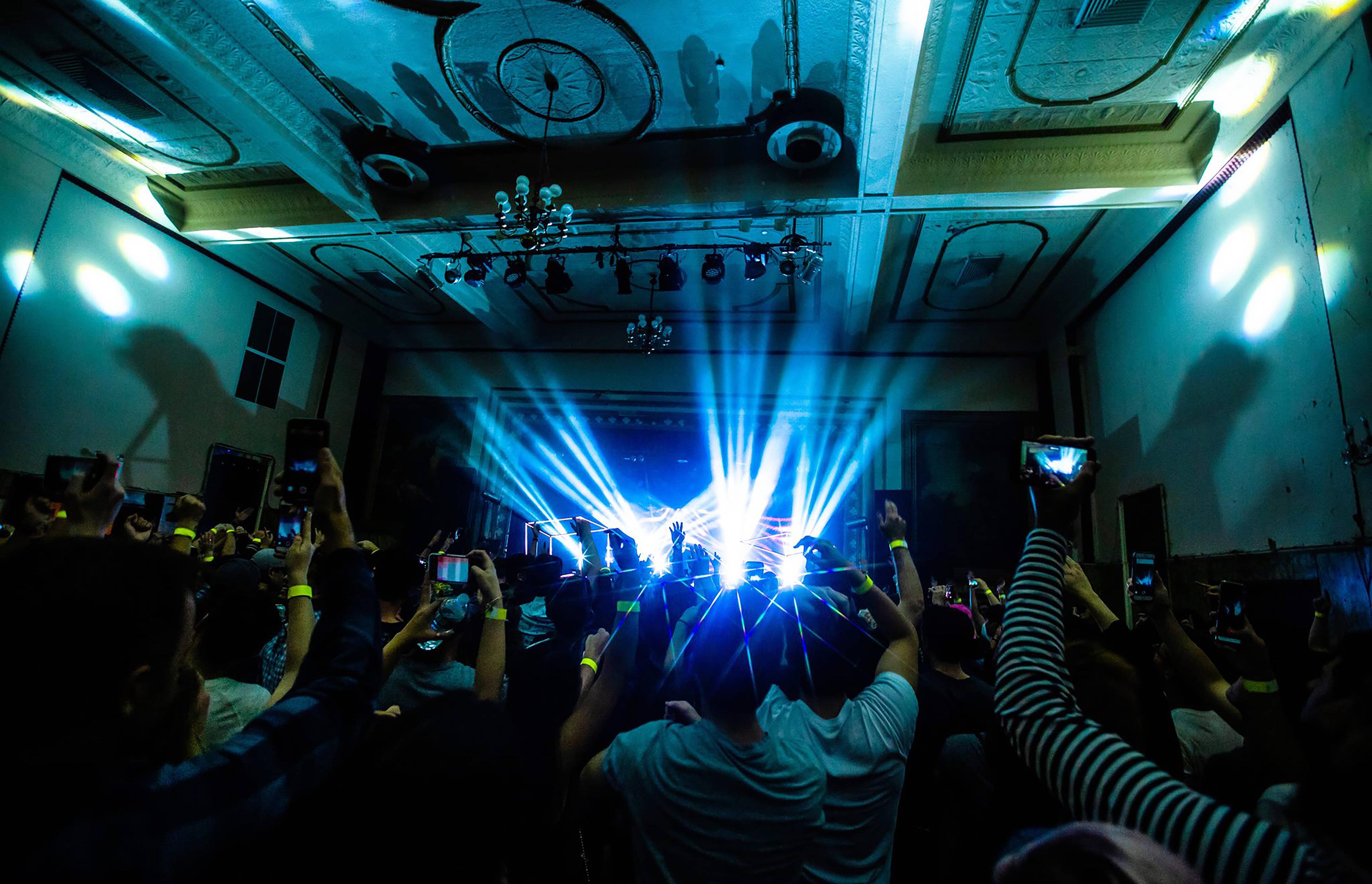 a photo of a fans facing the stage at a Warsaw concert with their arms raised 