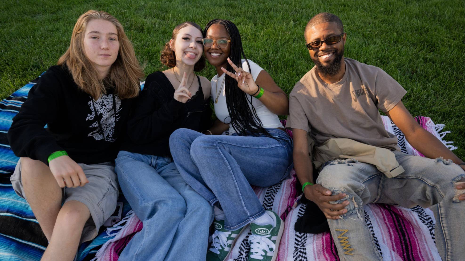 People are shown sitting on a colorful blanket on the grass