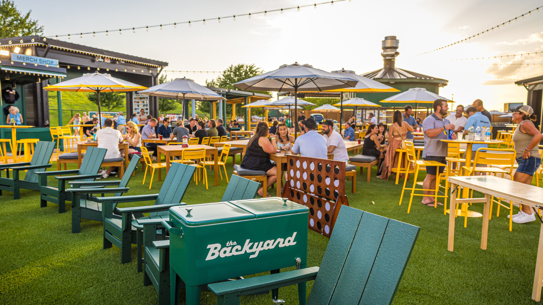 Concertgoers sit at picnic tables in The Backyard VIP Club eating dinner and playing lawn games.