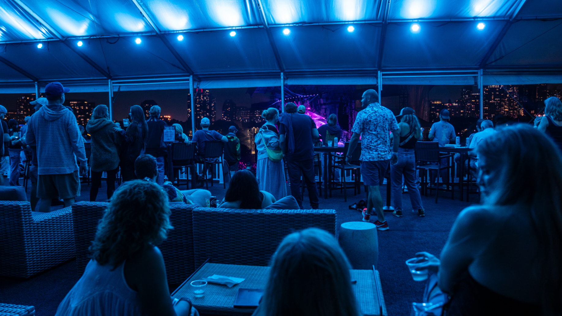 Fans sit on lounge chairs, while other fans stand on the platform looking out towards the stage and ongoing show. 