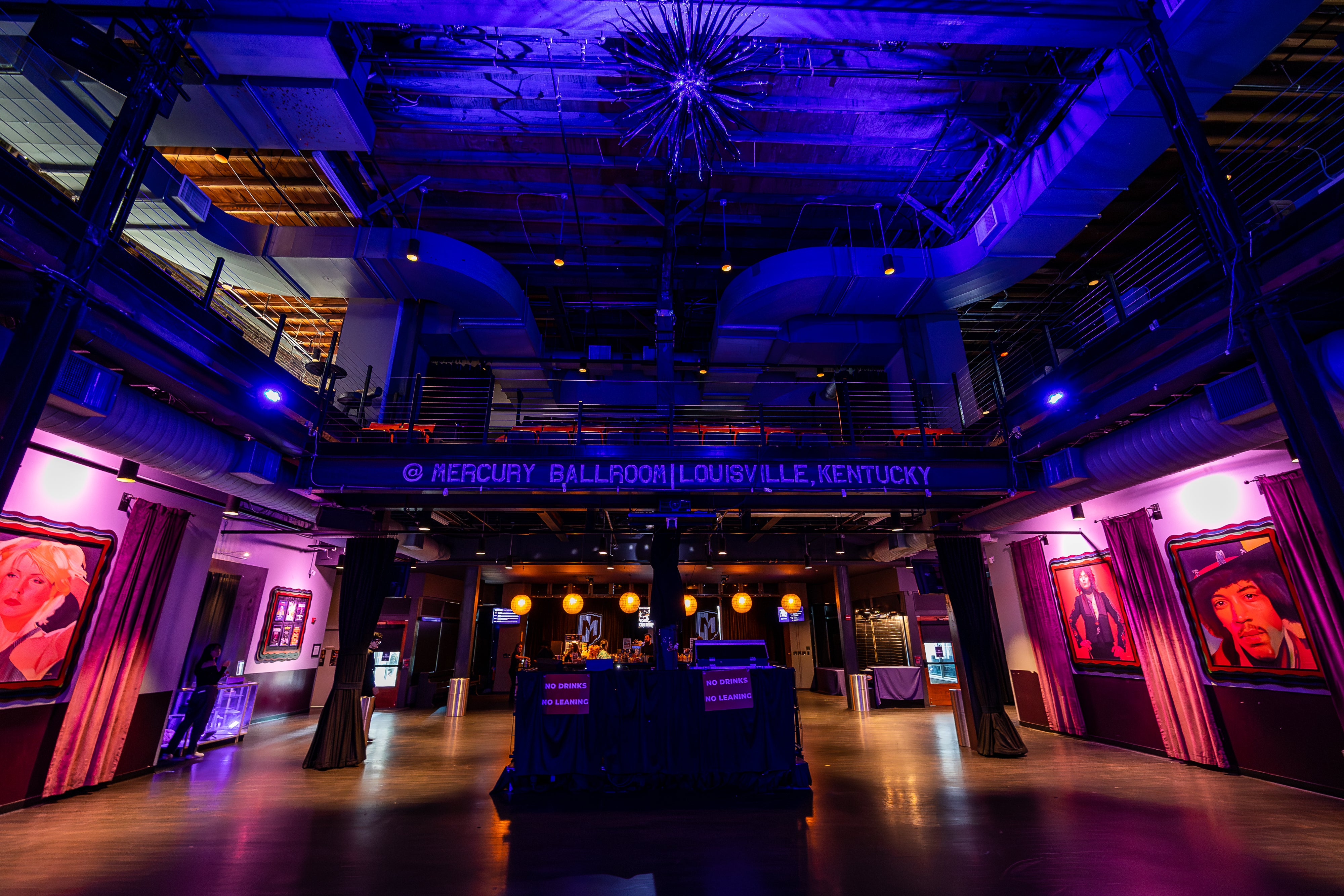 Mercury Ballroom interior with bold lighting, music portraits, a central bar, and an upstairs mezzanine.