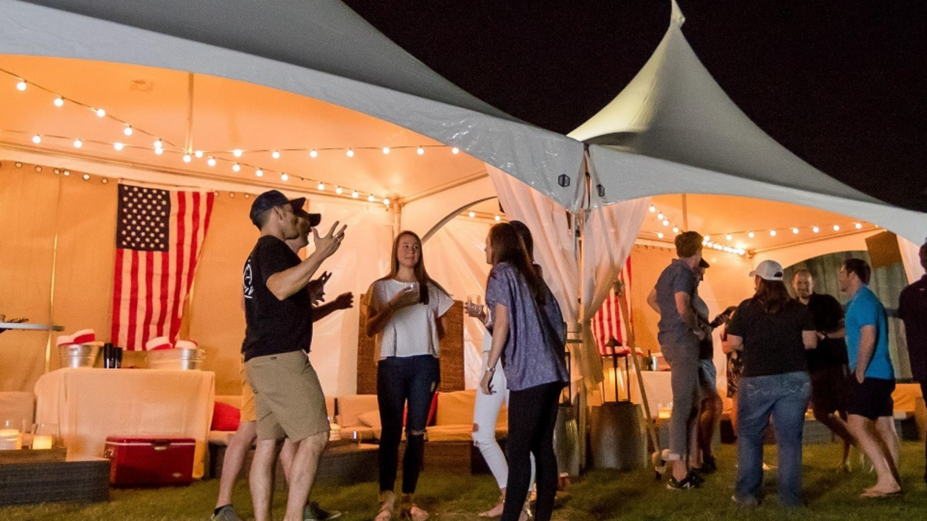 Fans stand in front of Cabanas with comfortable lounge seating. Fair lights hang from the top of the Cabanas. 