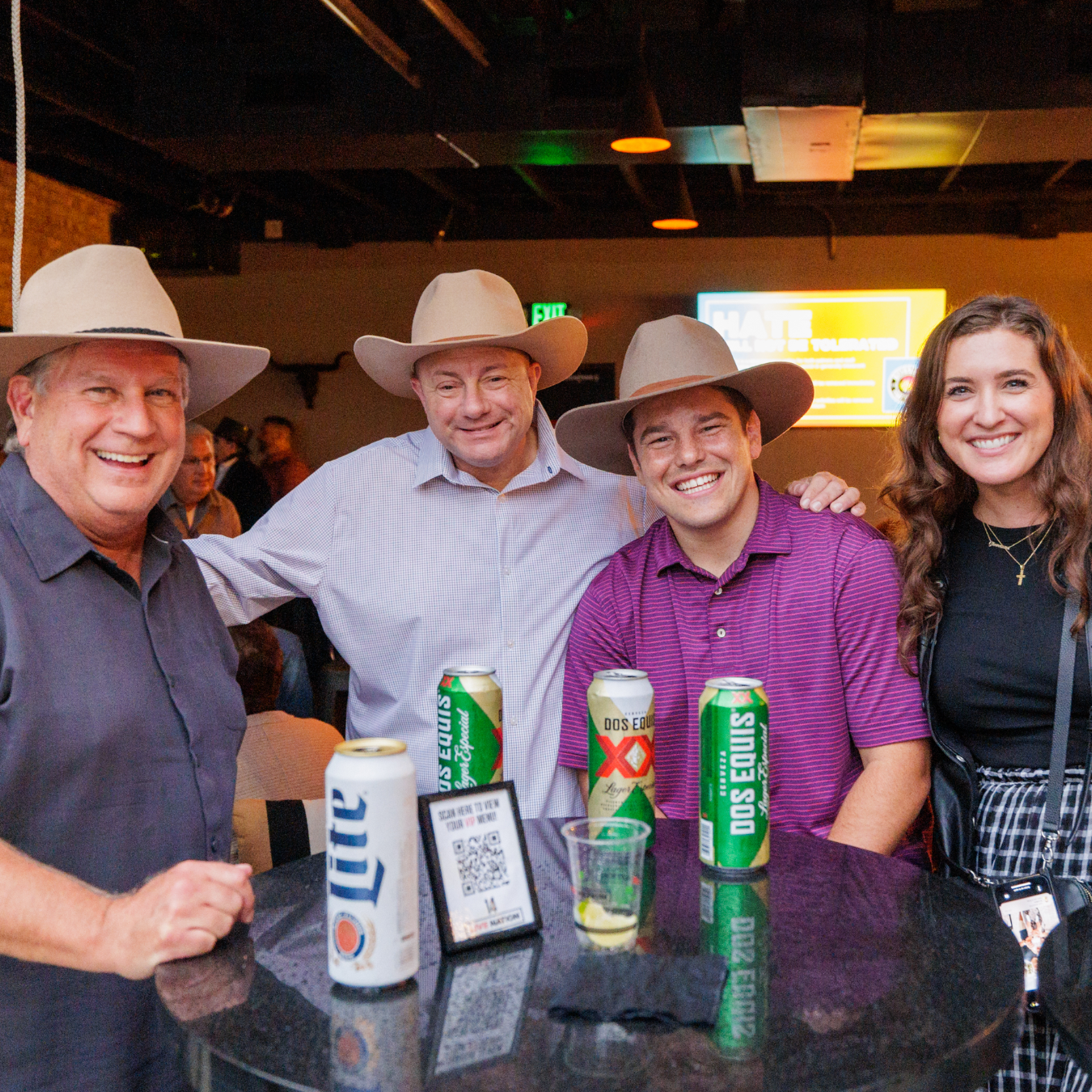 Three men in cowboy hats, one woman with long brown hair, standing at a table with drinks in the Citi Group Lounge.