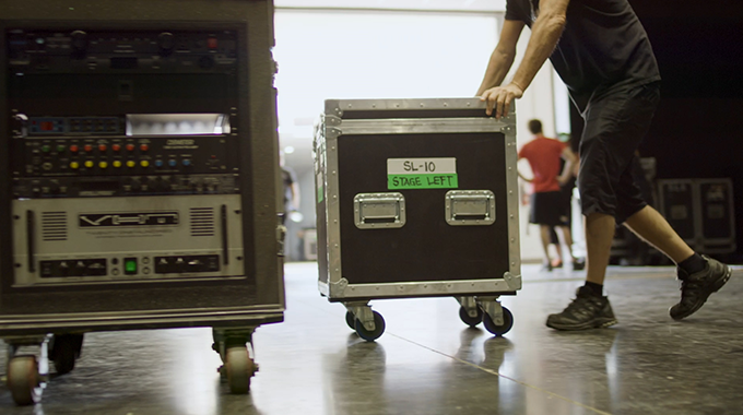 Crew member pushing professional audio equipment on rolling cart backstage