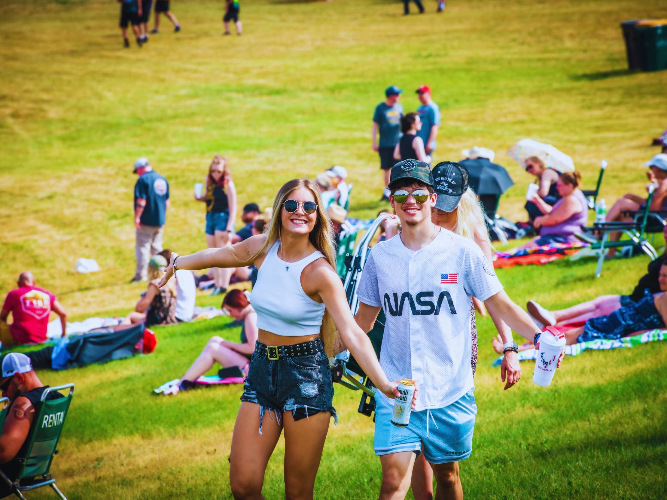 Two people with sunglasses smile at the camera while standing on green grass.