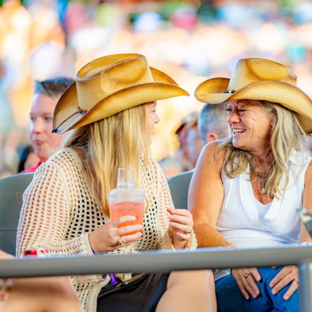 Two women in hats laughing, sitting in their seats at a show.