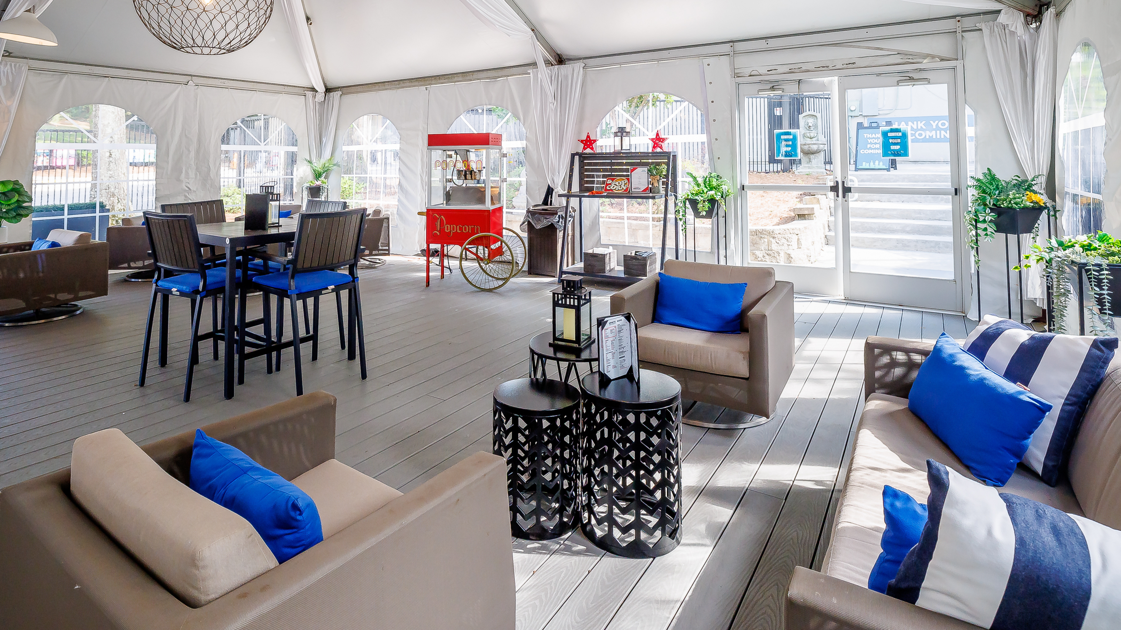 Covered VIP lounge featuring couches, tables, blue accent pillows, and a popcorn station