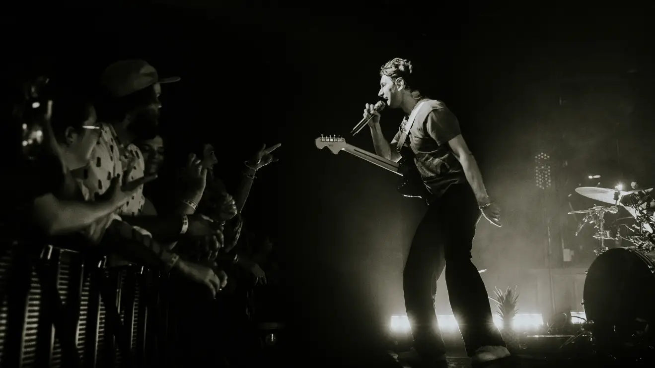 Photo of Glass Animals on stage performing at The Underground with people singing along the barricade. 