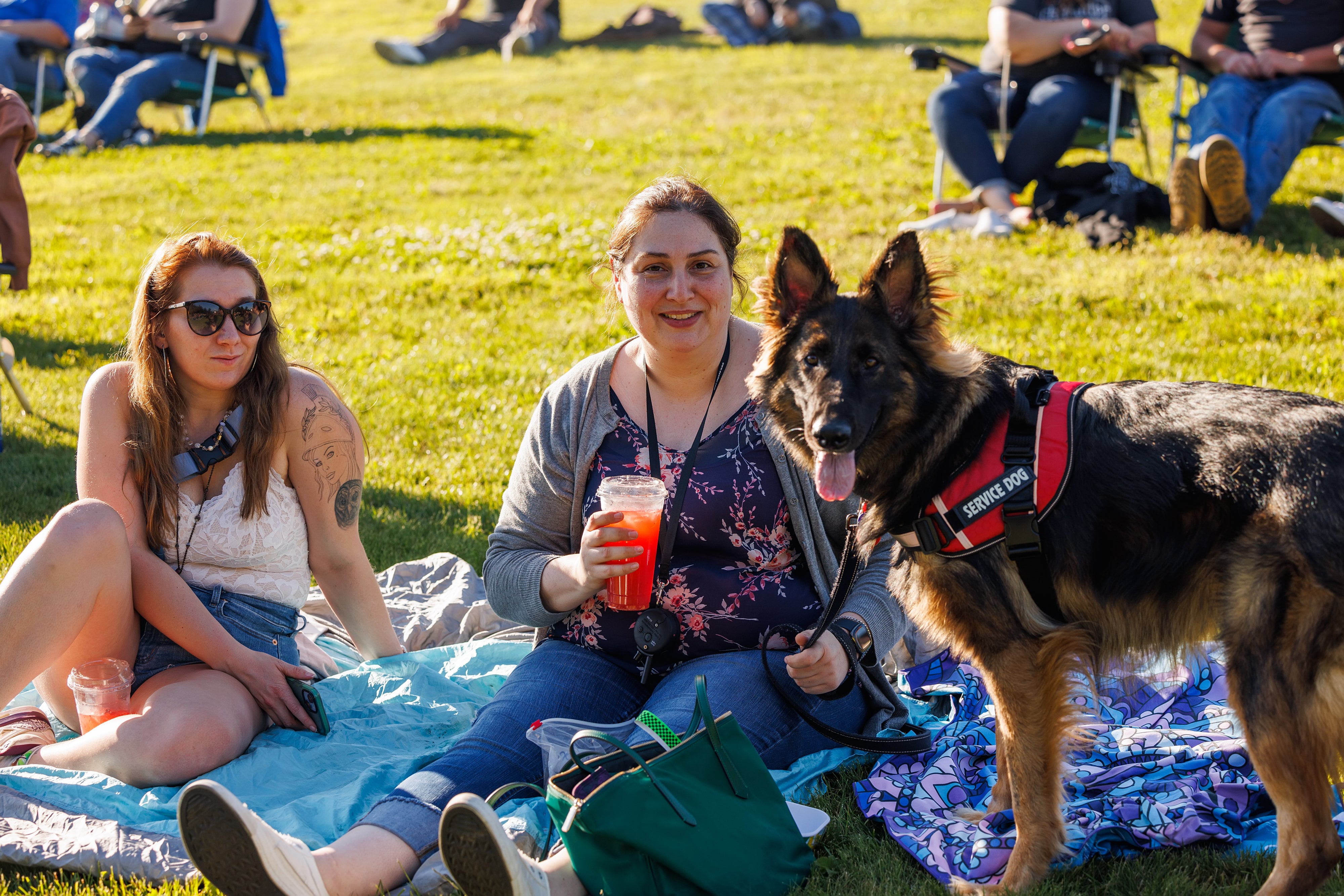 Fans smiling on the lawn with a drink and their service dog 