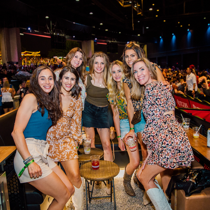 A group of girls smiling for a picture in a VIP box during a show
