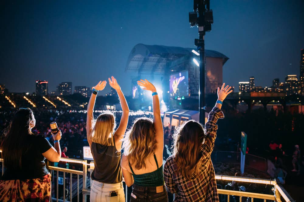 Three women wave their hands in the air while watching a concert.