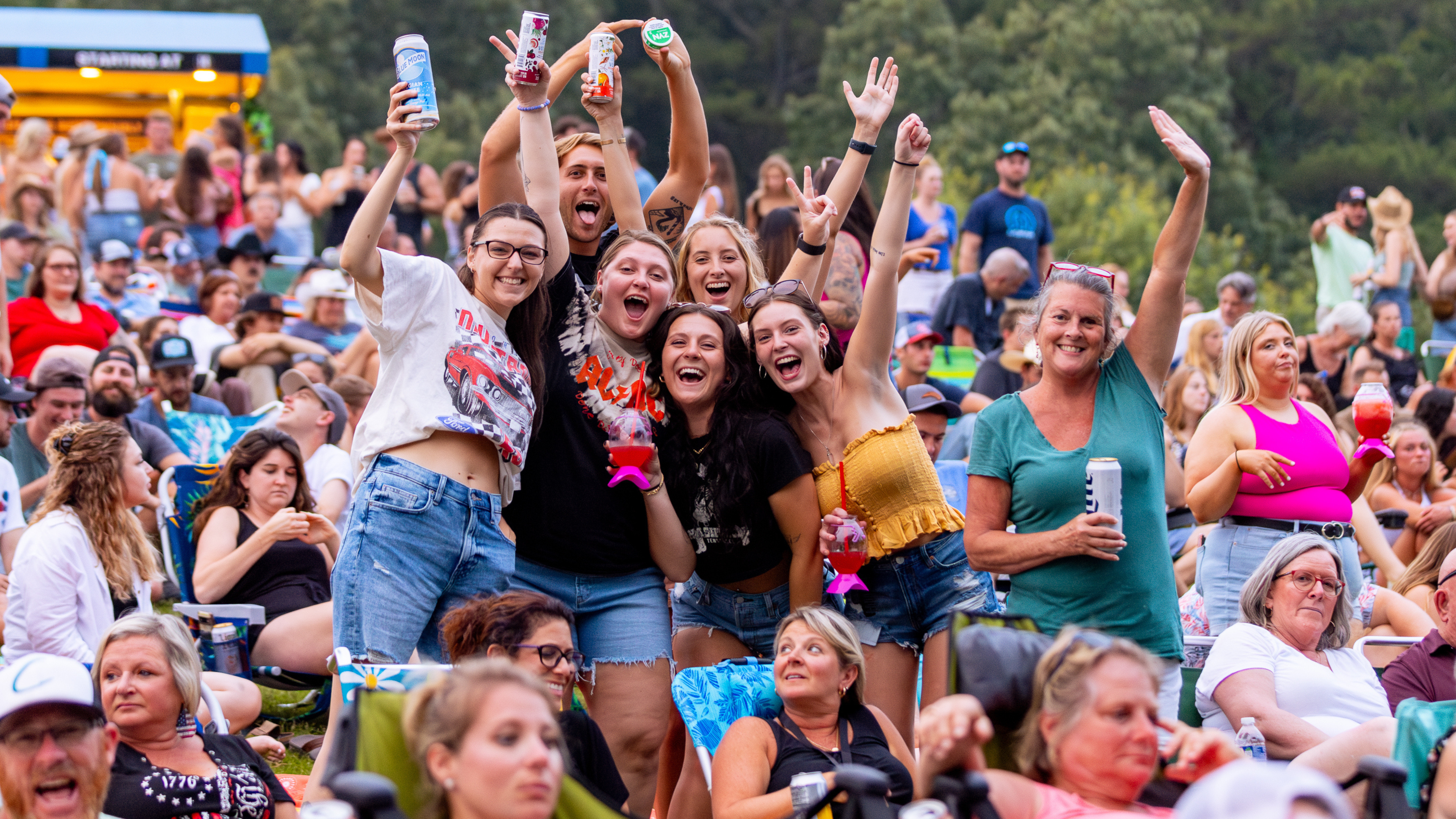 A photo of 7 people smiling with their hands in the air on the lawn