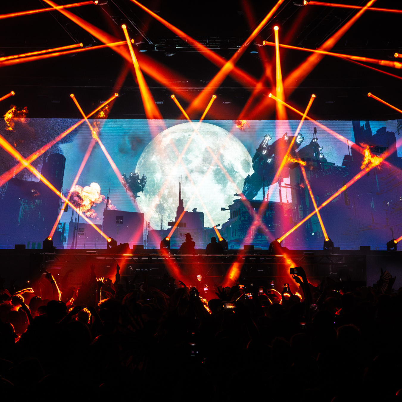 The stage during a performance, with orange lasers and a full crowd, silhouetted.