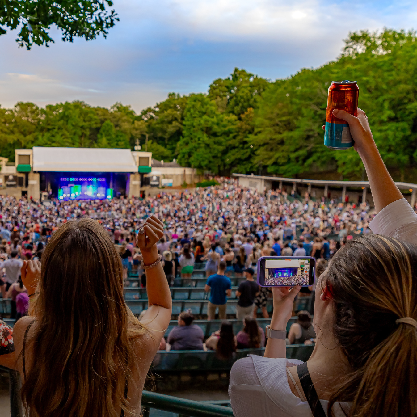 Two women cheering and raising their drink at a concert.