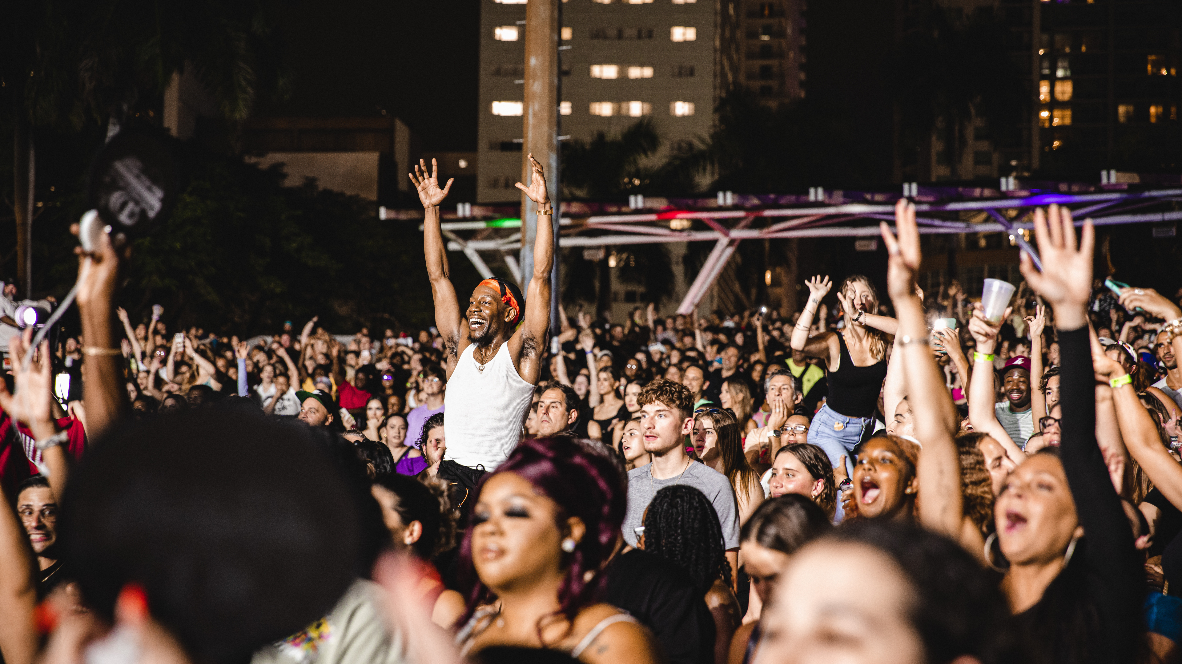 A lively crowd at FPL Solar Amphitheater cheers and raises their hands during a night performance, with fans showing excitement and energy under city lights.