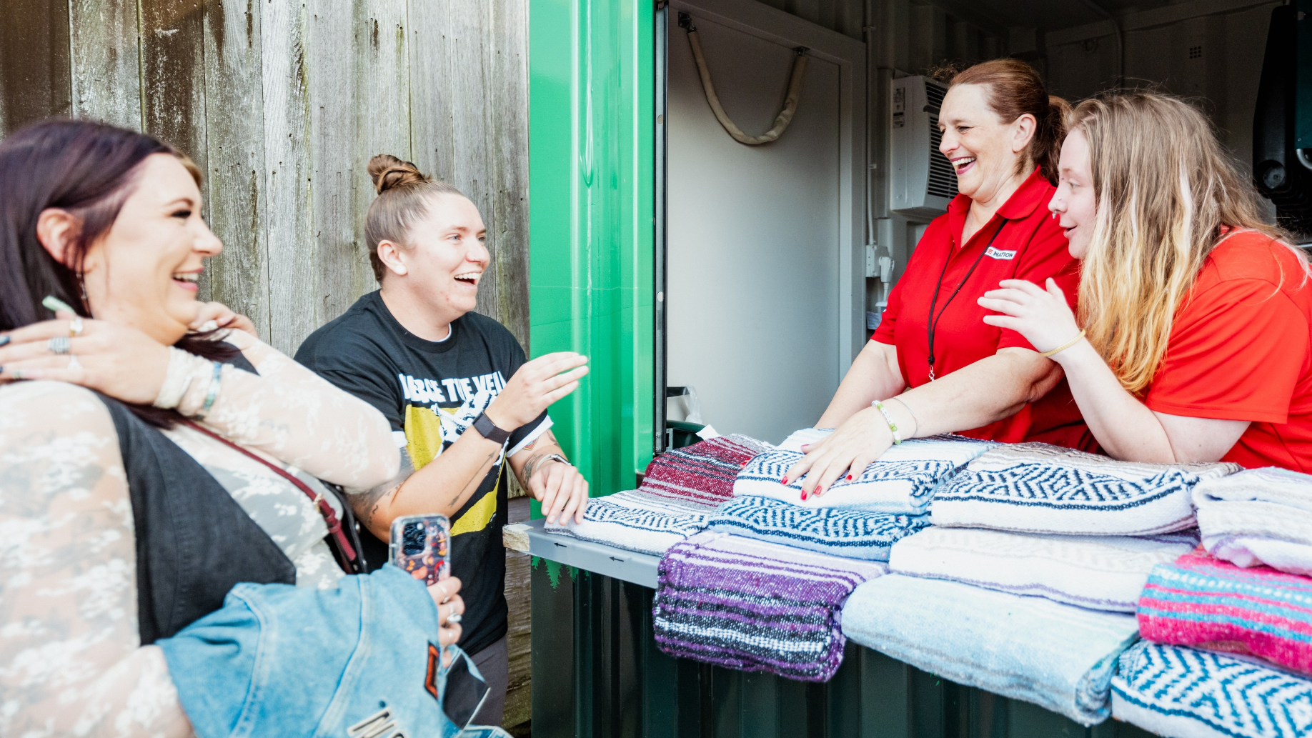 Two employees smiling and talking with fans at the blanket rental stand. Multiple blankets on display in front of them.