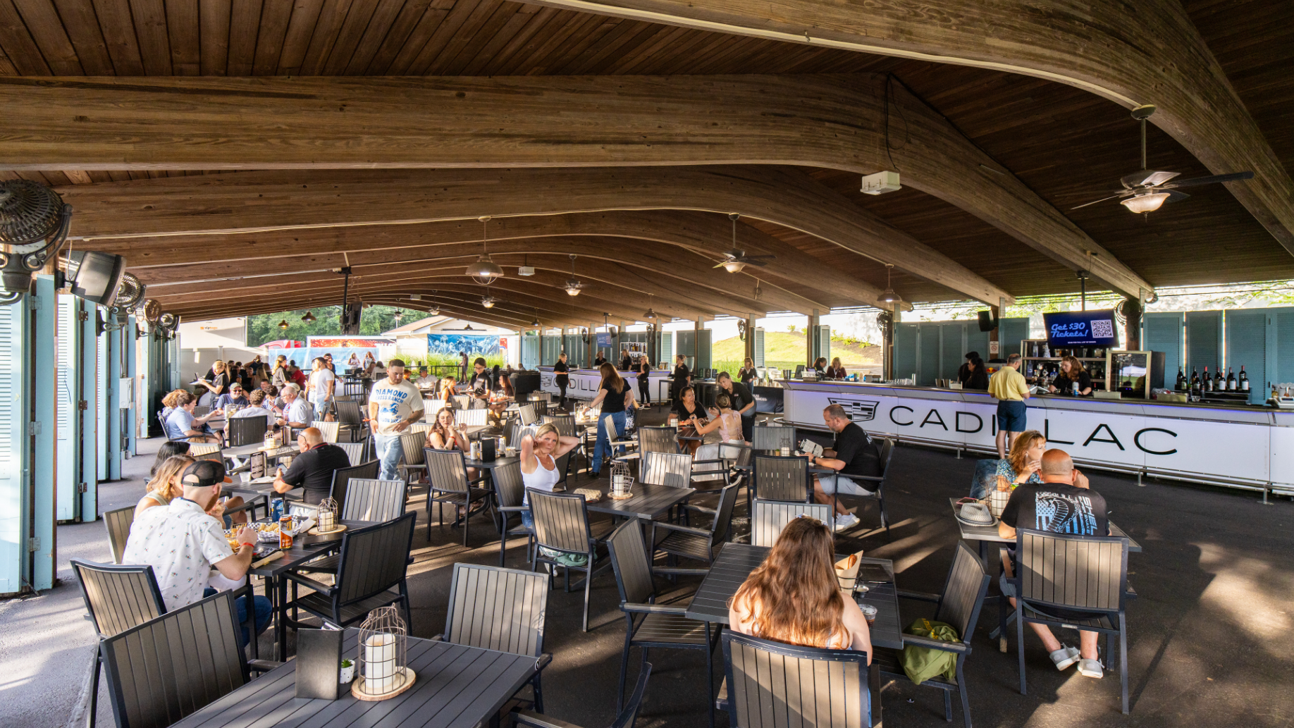 The VIP Club at PNC Bank Arts. Fans sit around tables in a shaded lounge area, featuring a private bar. 