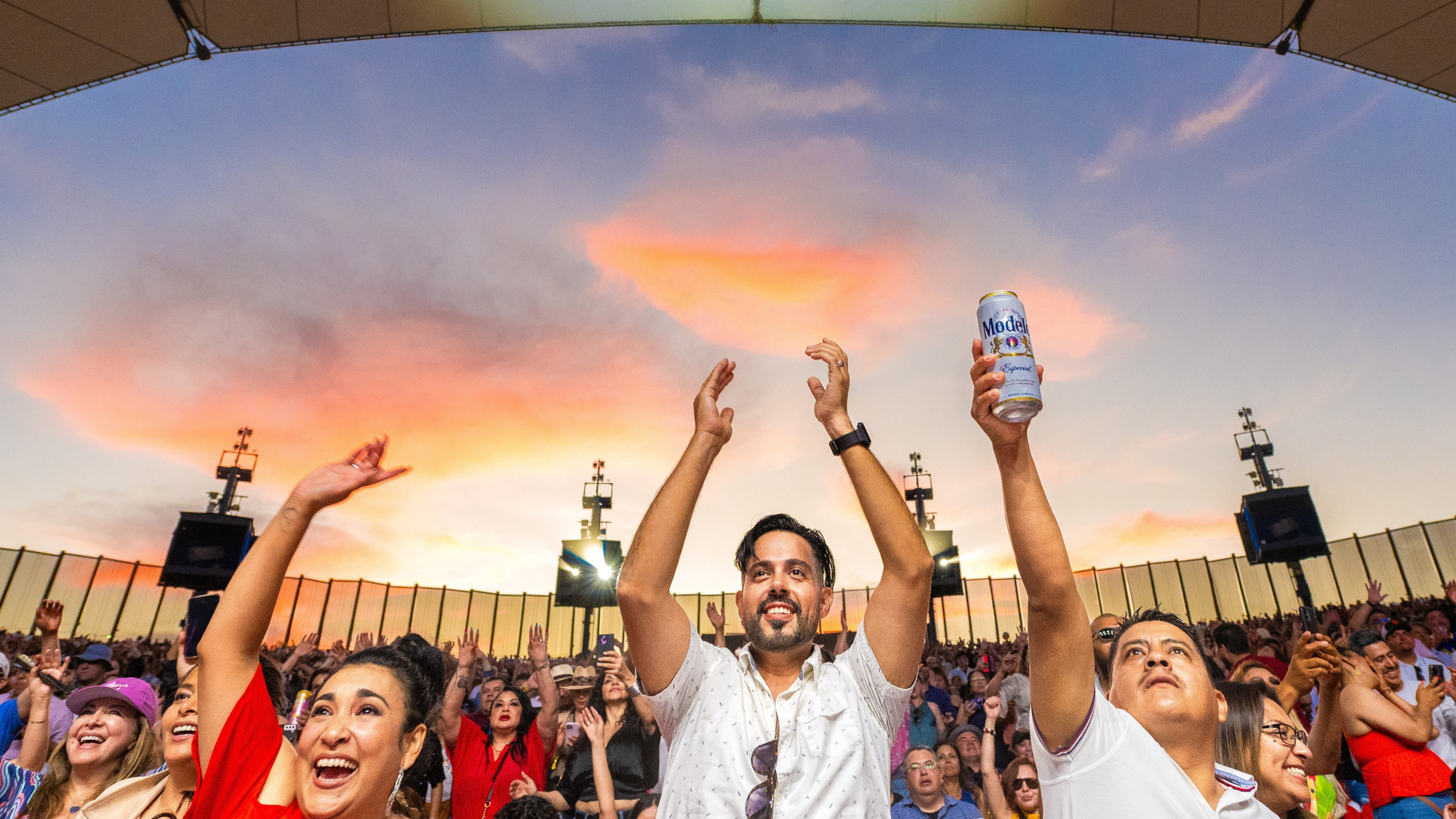 Fans standing, clapping and dancing with their arms in the air with the sunset in the background