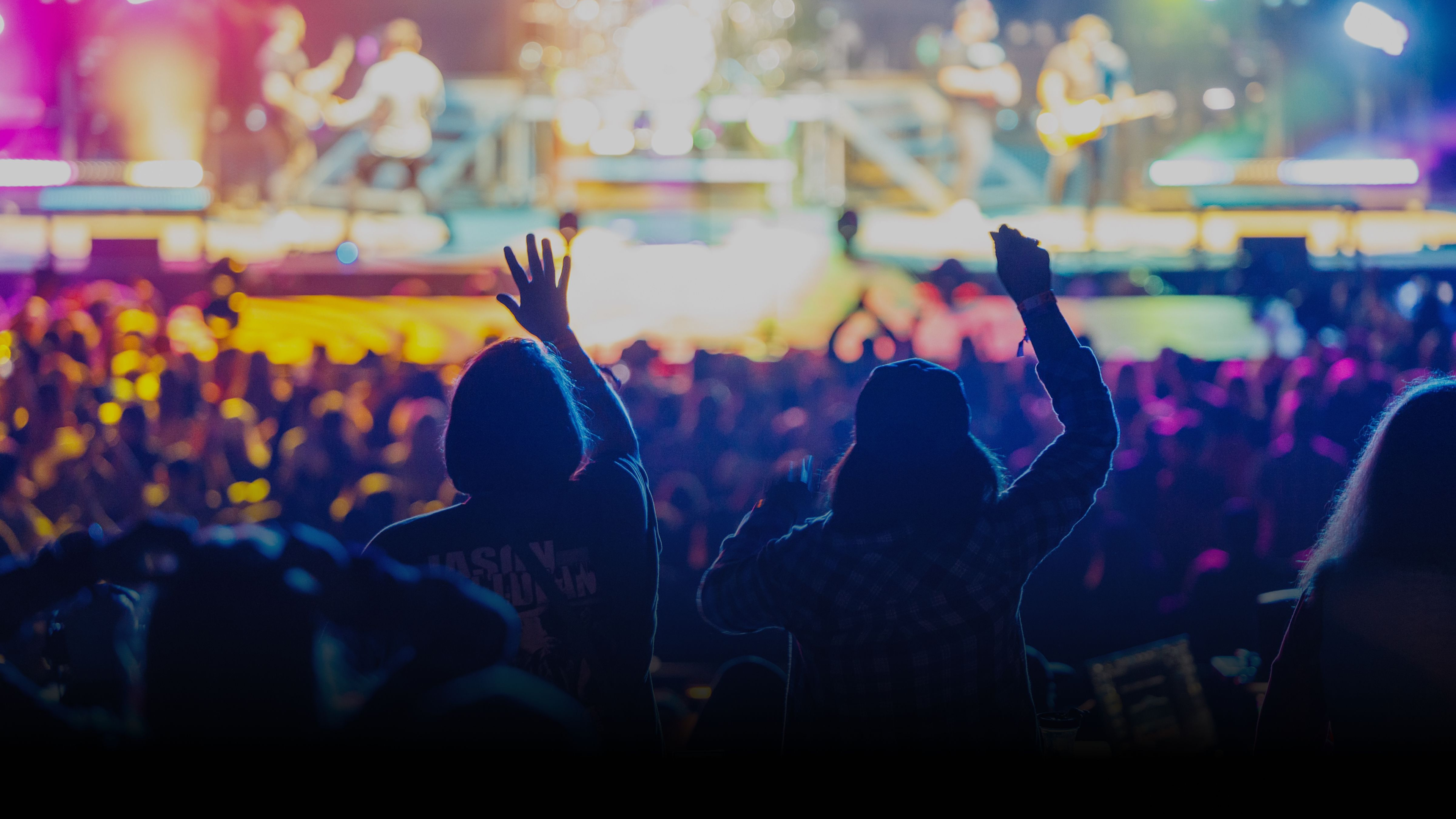 Two fans are enjoying a concert with their hands in the air