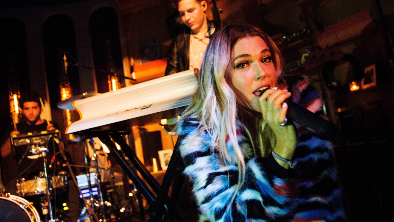 A woman singing into a microphone on stage looking at the camera