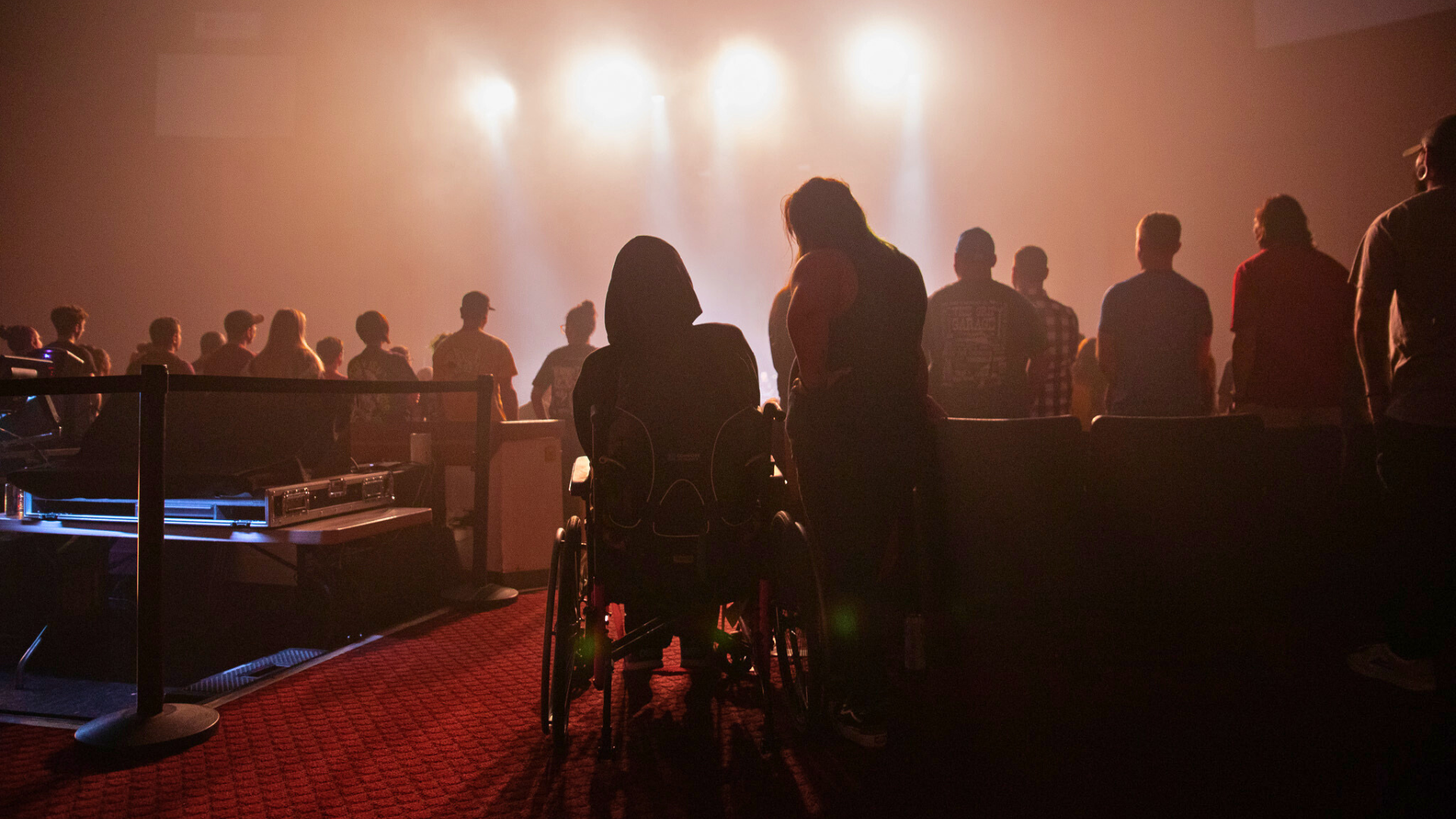 A fan in a wheelchair accompanied by a friend standing and watching the show