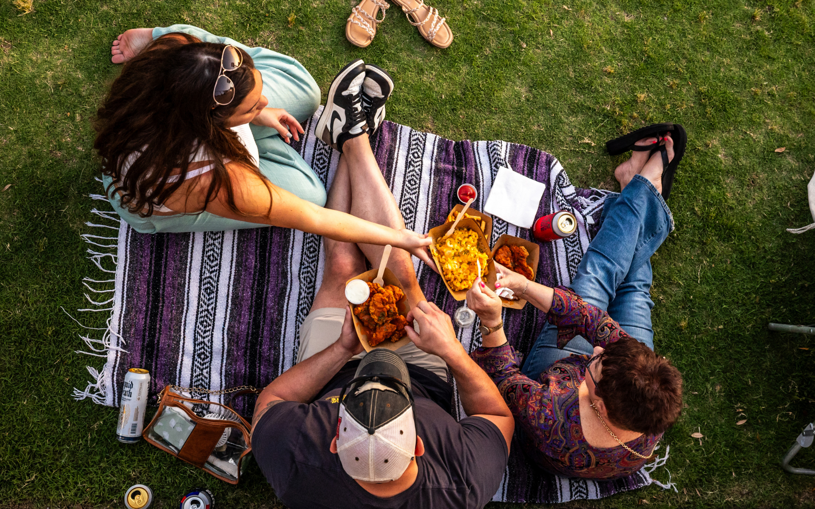 Fans sitting on a blanket in the lawn enjoying food and drinks.