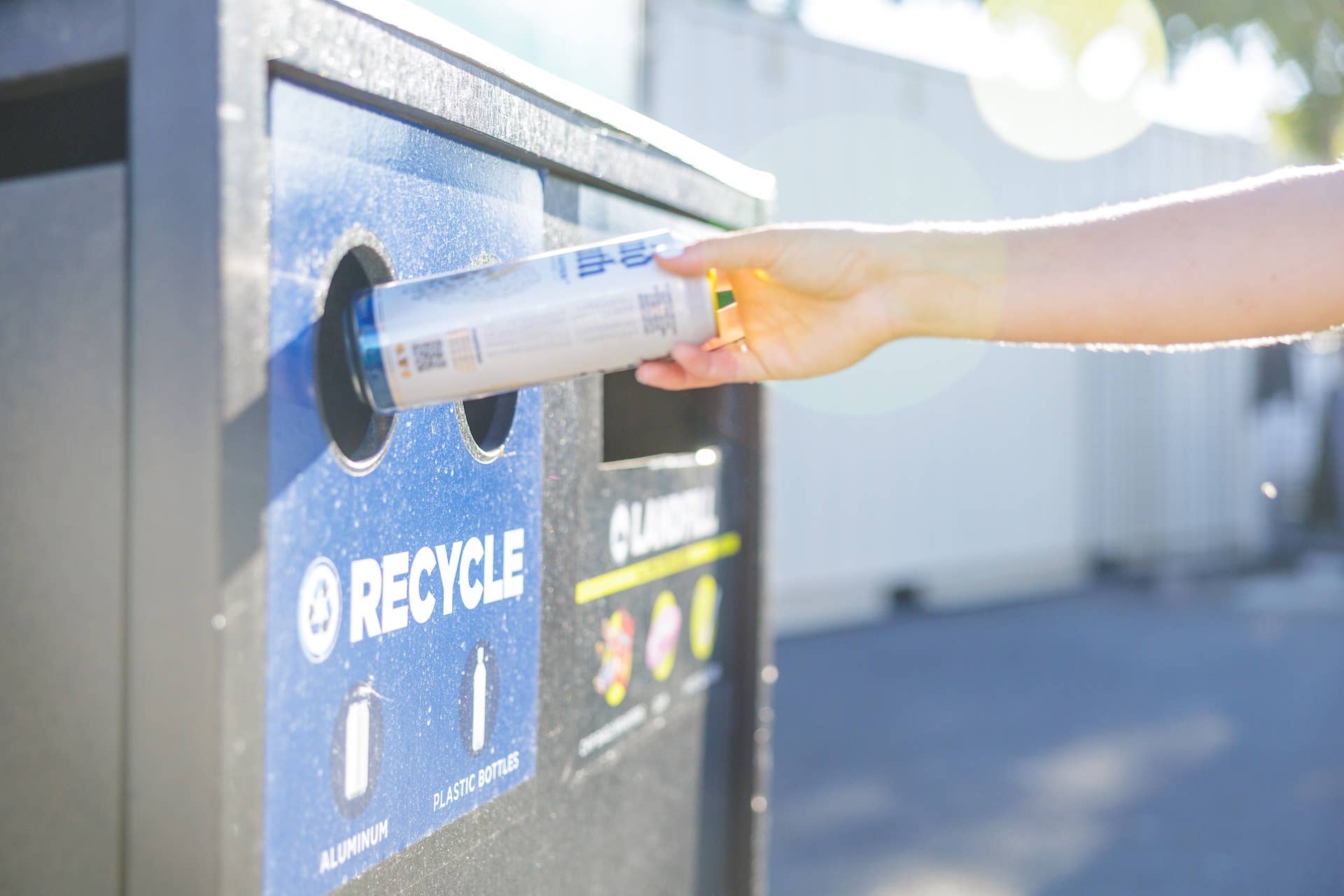 A person places a can into a recycling bin.