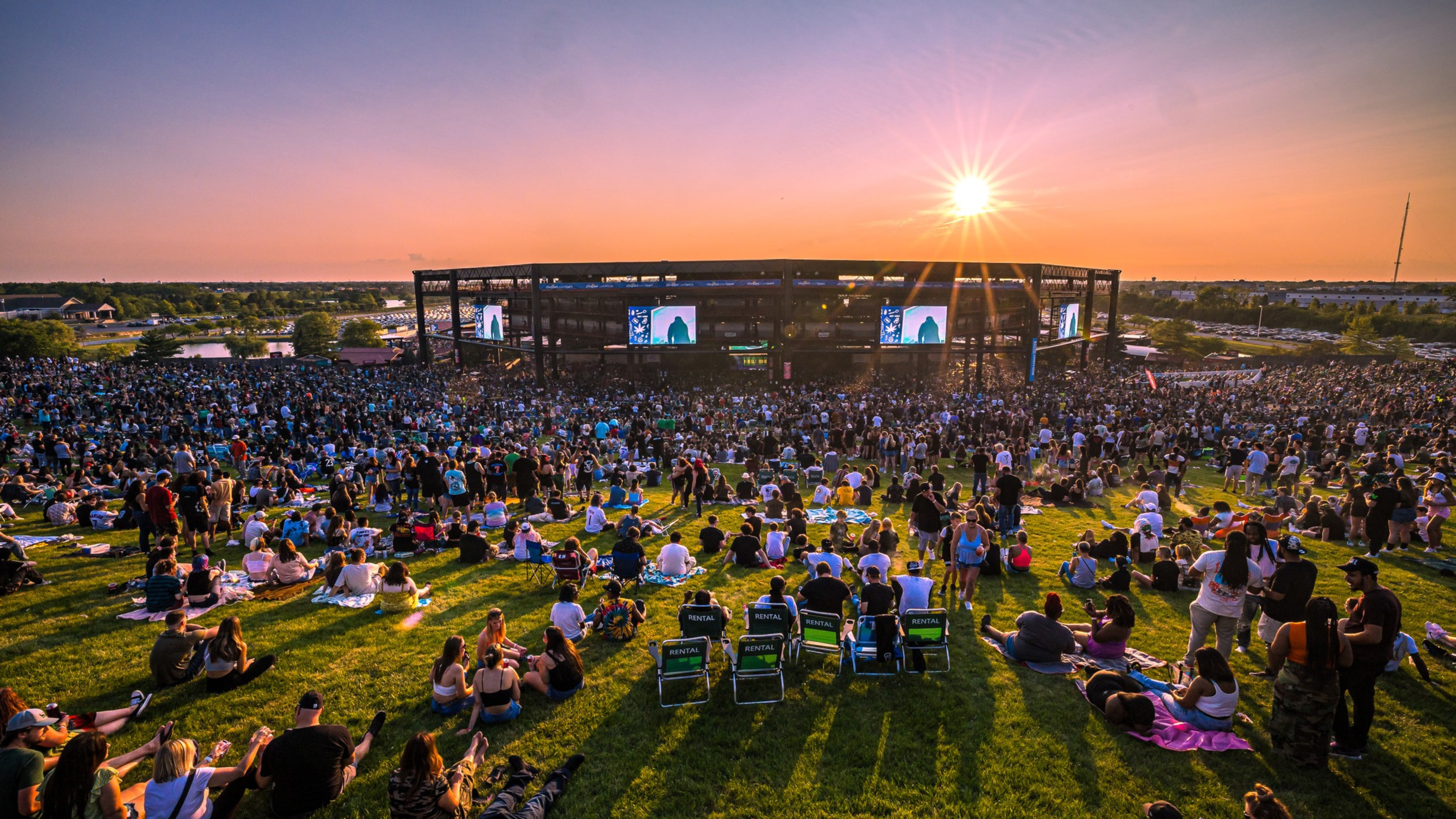 A large crowd of fans sitting on the lawn watching a show at Credit Union 1 Amphitheatre.