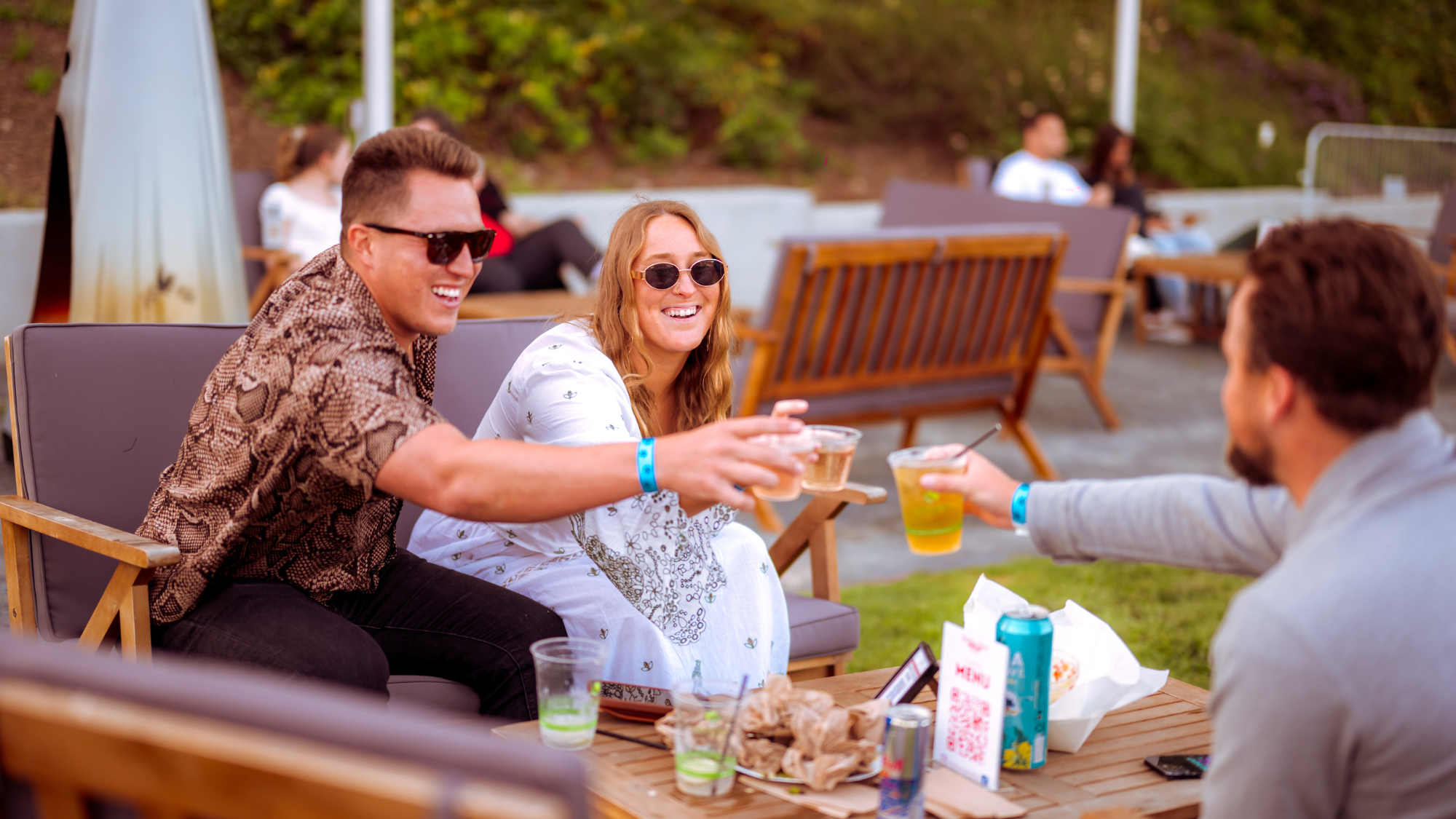 Three people sit in plush lounge sofas and cheers their wine and beer.