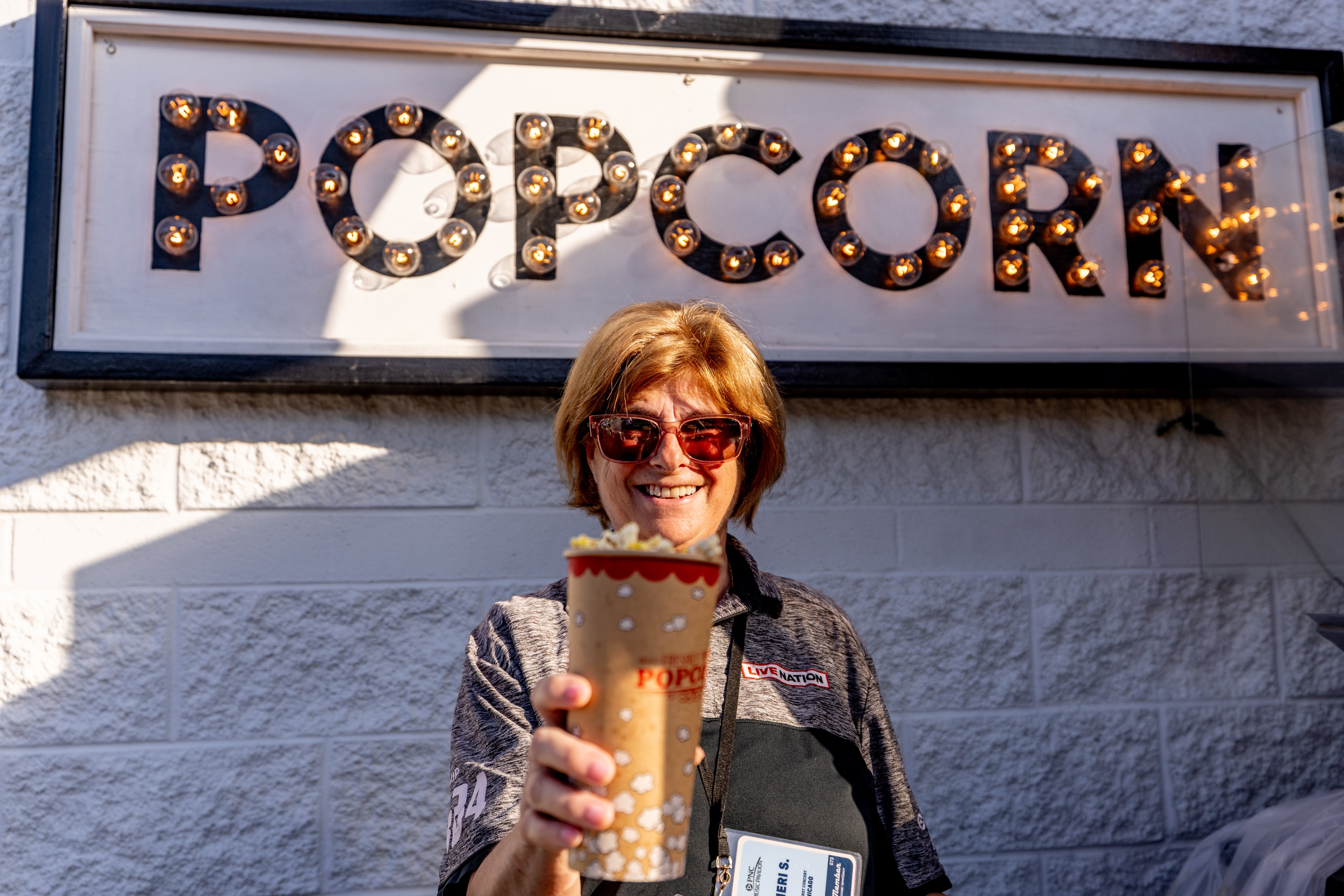A premium employee holding up popcorn in front of the popcorn sign. 