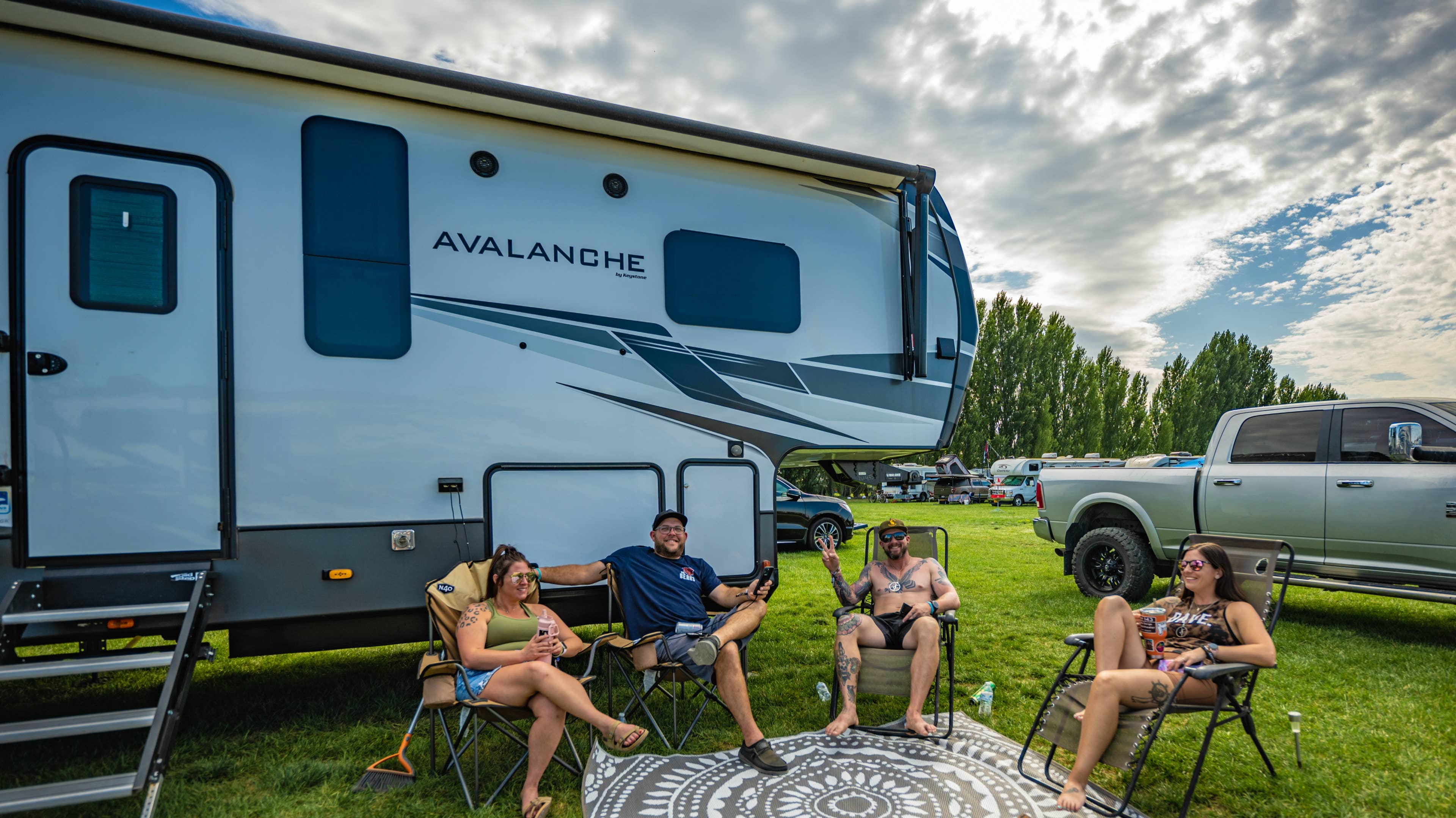 An RV parked on a lawn with people sitting outside in their portable camping chairs