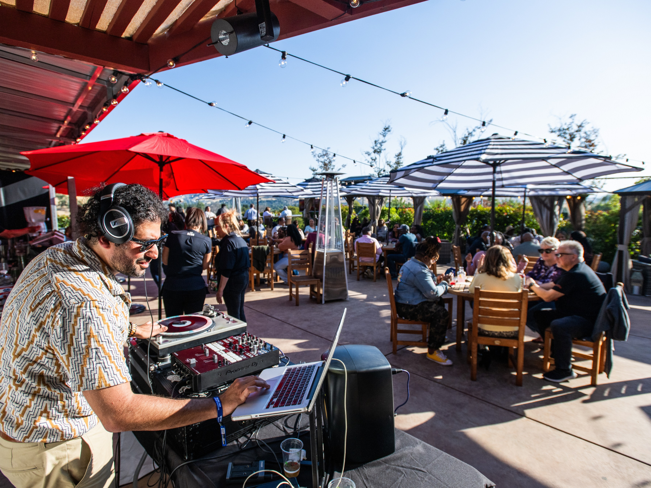 VIP Club with DJ playing music and people sitting, eating and drinking at tables under large umbrellas