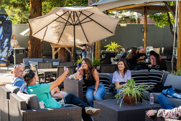 4 people sitting on patio furniture in a VIP club under a large umbrella having a friendly conversation