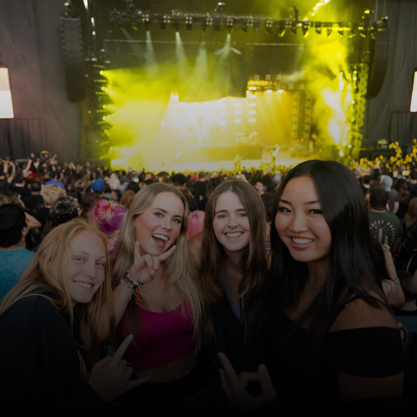 Four young women smile at the camera while the stage is lit up behind them