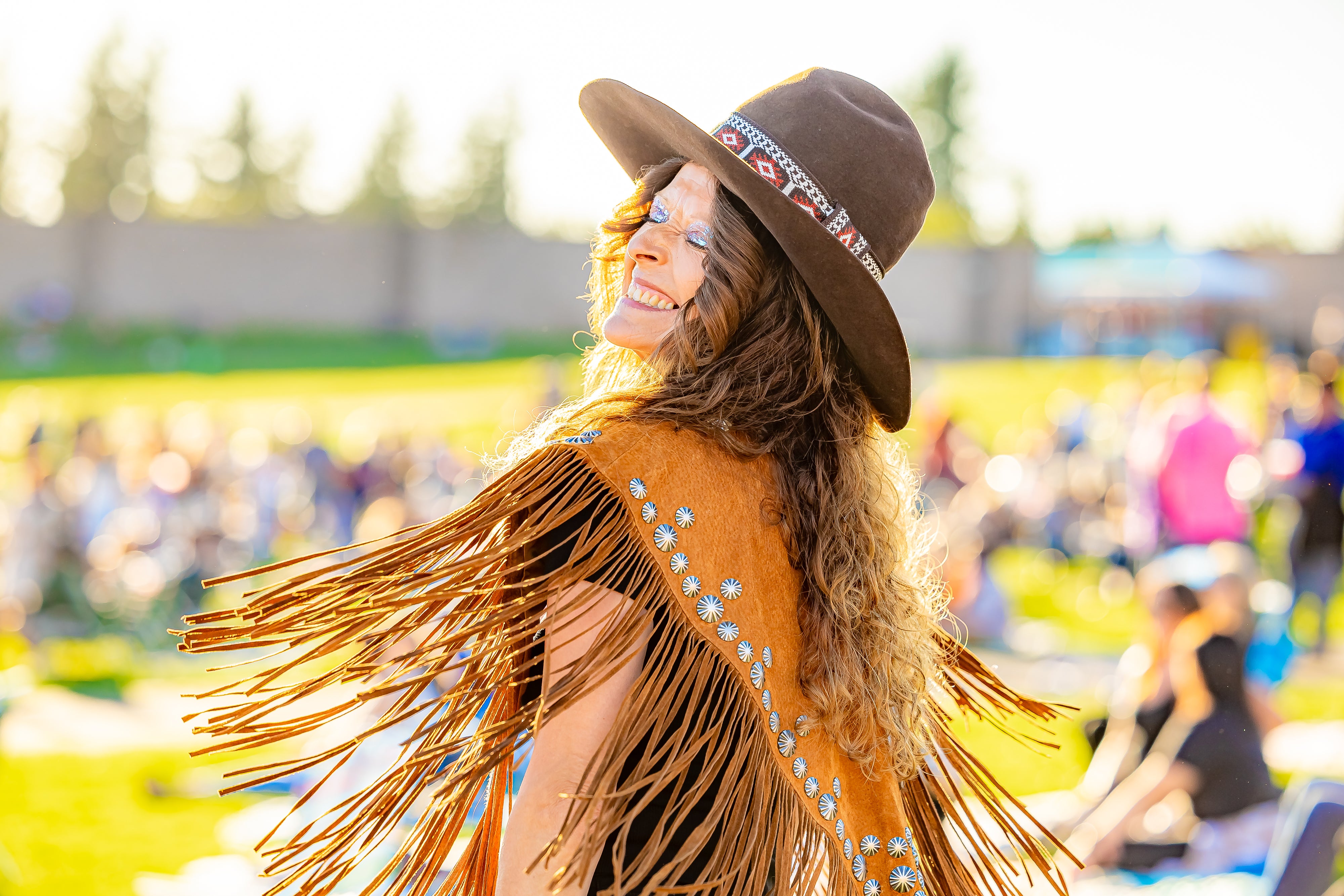 A woman wearing a fringe vest and a hat smiling and twirling