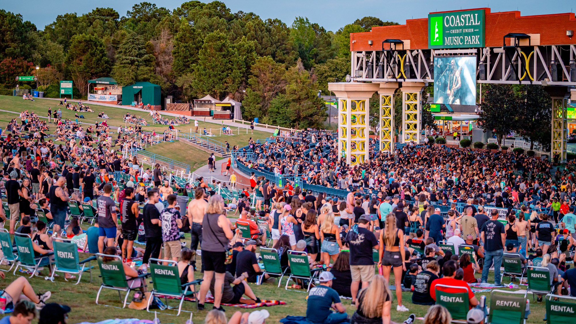 A crowd in the lawn at a concert. People are sitting in lawn chairs and standing.