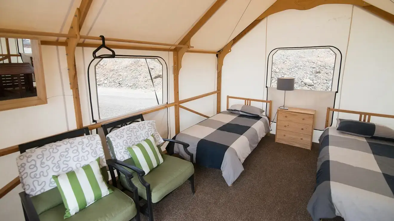Cottage-style tent comes complete with bedding, furniture, a cooler, fan, lamp, and power for cell phone charging.