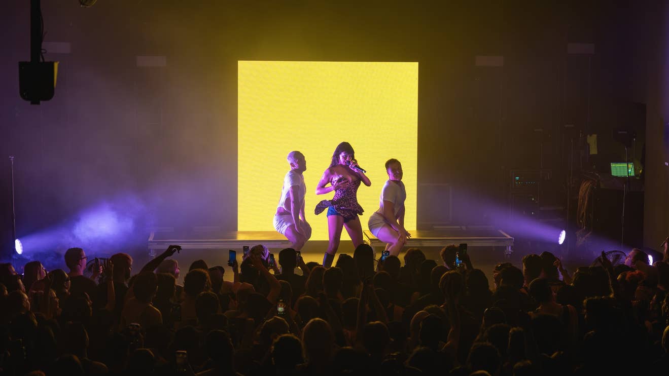 Artist on stage at The Mod Club in Toronto singing into a microphone with background dansers posing beside her