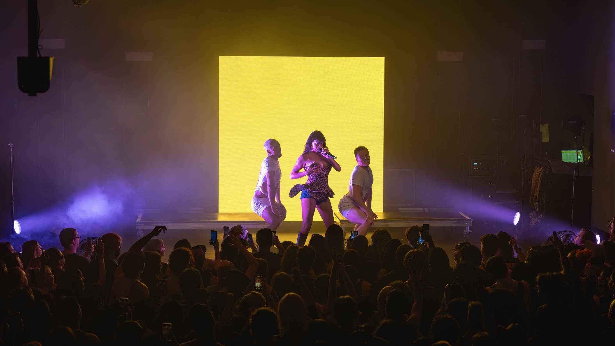 Artist on stage at The Mod Club in Toronto singing  into a microphone with background dansers posing beside her