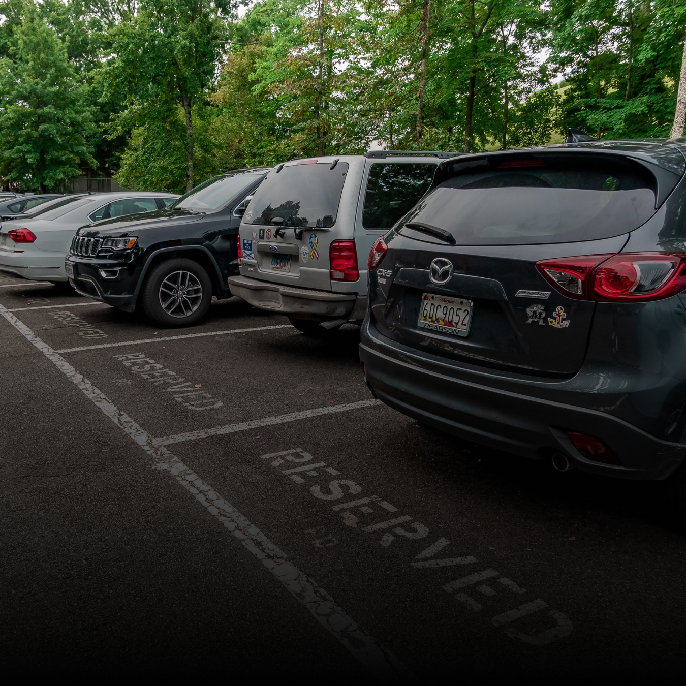 Four cars parked in an outdoor parking lot in reserved spaces.