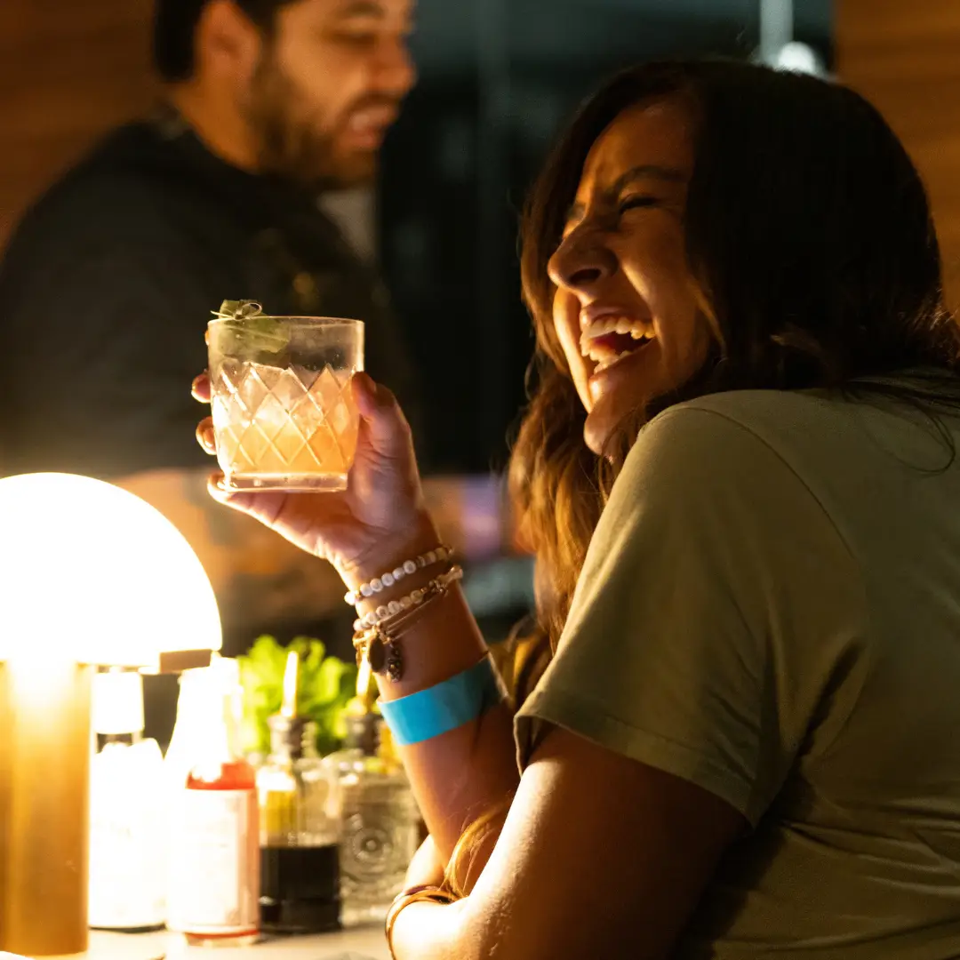 A woman is enjoying a drink and smiling at Good Luck Lounge
