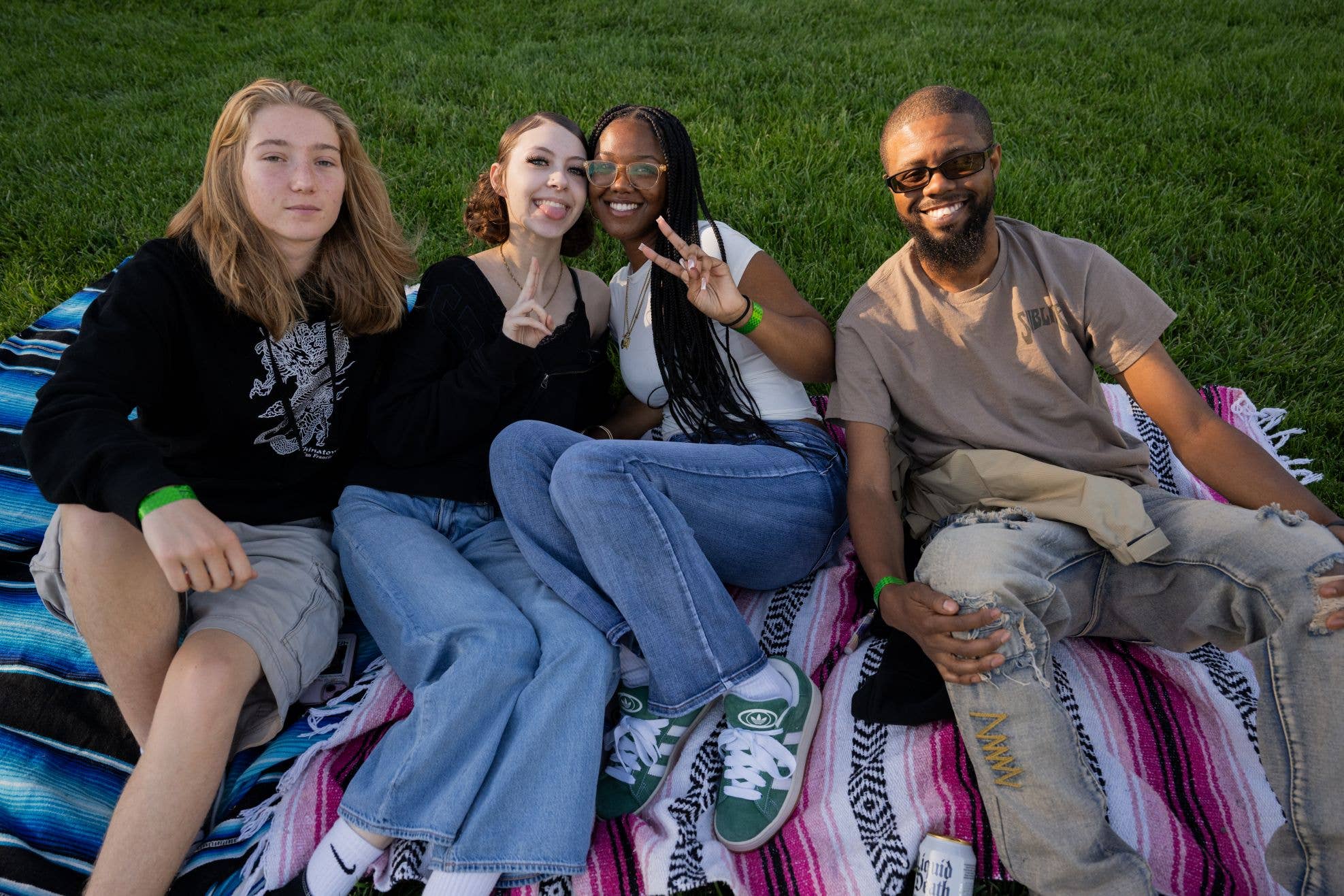 People are shown sitting on a colorful blanket on the grass smiling