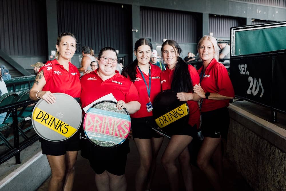 A group of female wait service employees smiling for the camera while holding up "drinks" signs