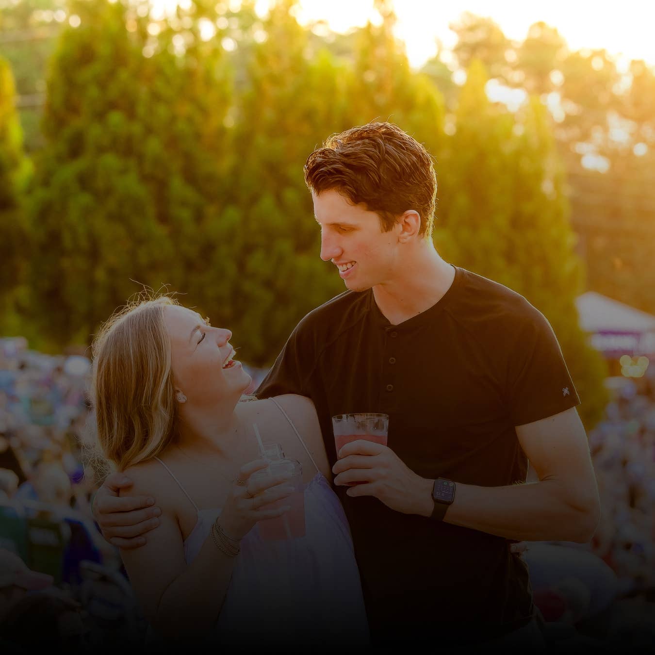 A couple smiles at each other in front of trees.