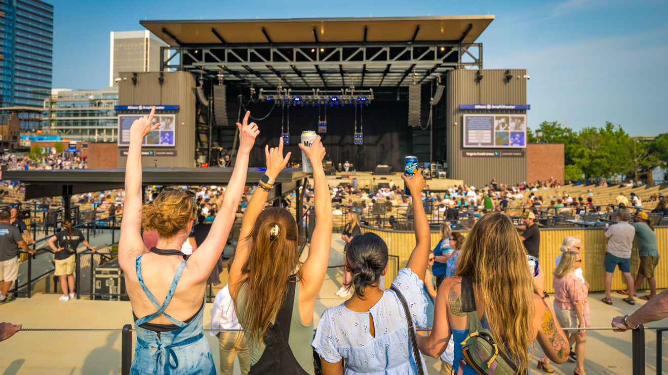Four female fans look on at the stage raising their drinks.