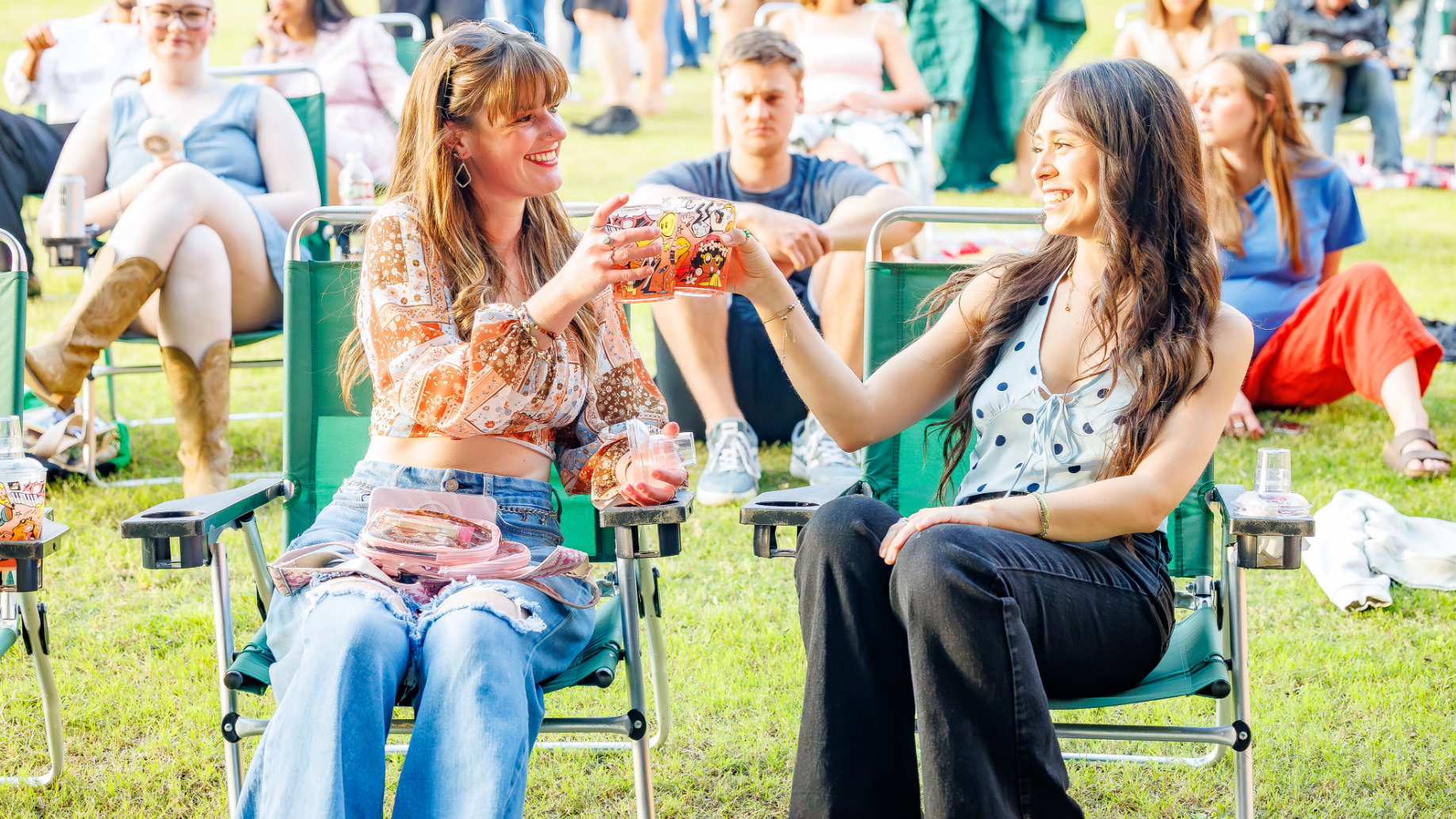 Two girls sitting in rental lawn chairs smiling and enjoying their drinks.